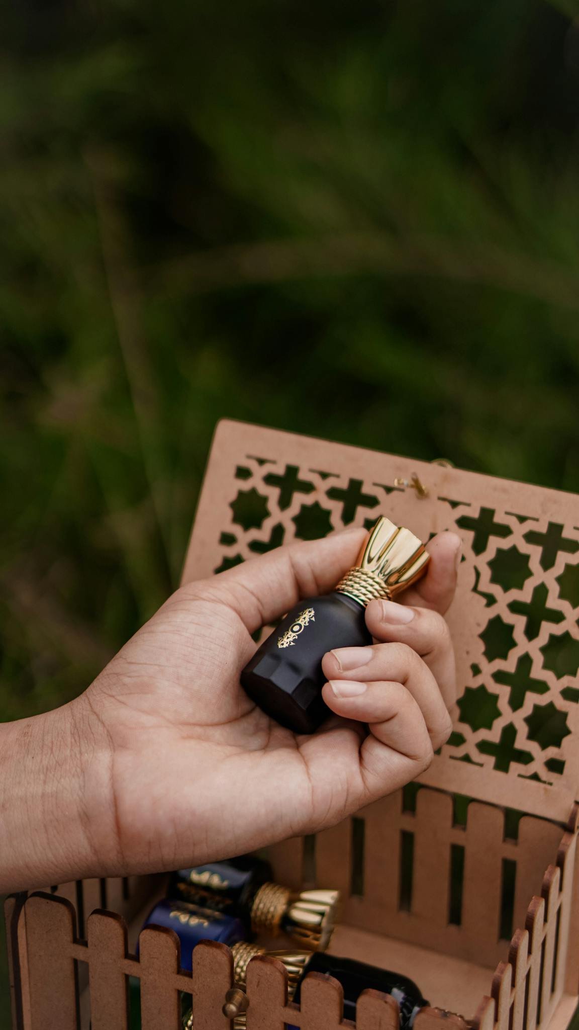 Close-up of a hand holding a black perfume bottle with a gold cap, showcasing elegance.